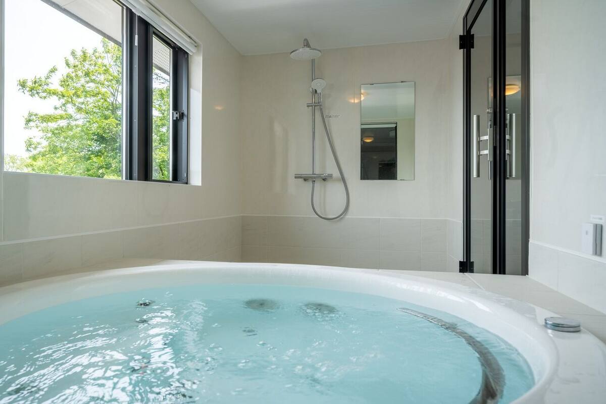 A modern bathroom with a large bathtub, a shower, and a window providing natural light.