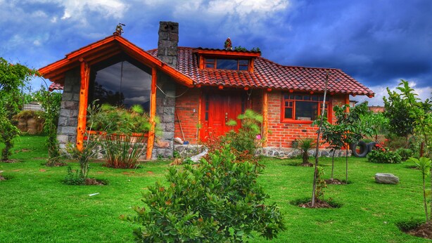 A rustic house with a red-tiled roof, stone walls, and a large glass window. - Kalera Lodge - Equator Face (Cotacachi)