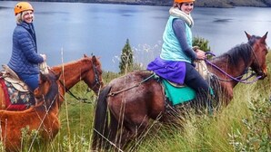 Two people riding horses on a grassy area with a lake in the background. - Kalera Lodge - Equator Face (Cotacachi)