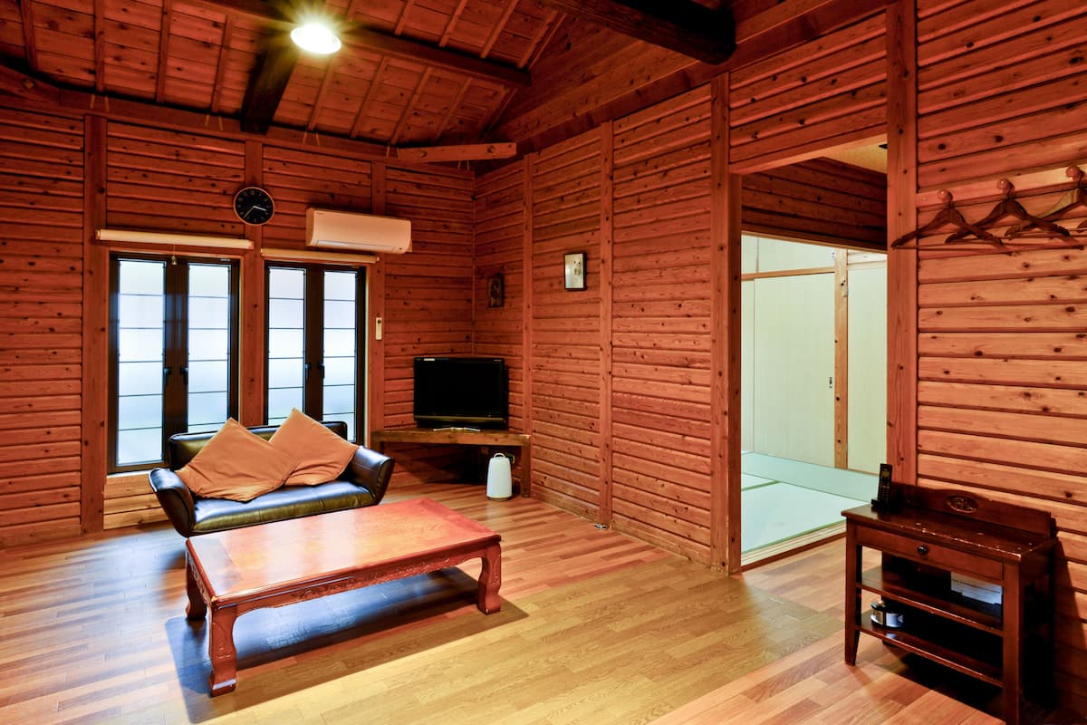 Interior de uma cabana de madeira com sofá, mesa de centro, televisão e porta de correr.