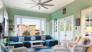 Un salon chaleureux avec un canapé bleu, des fauteuils en osier blancs et un ventilateur de plafond.