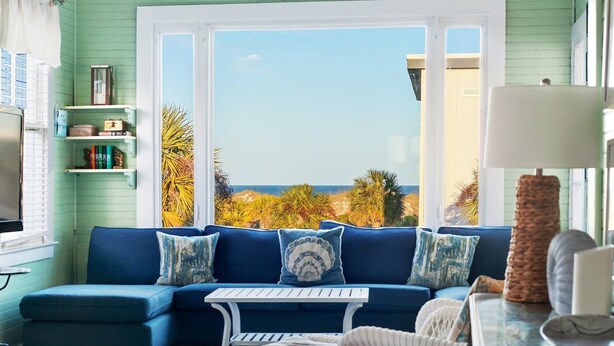 Une pièce avec un canapé bleu, une petite table, des chaises en osier, un téléviseur et une vue sur la plage.