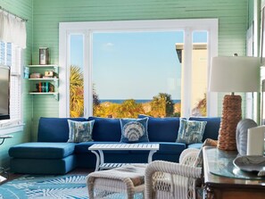 A room with a blue sofa, a small table, wicker chairs, a television, and a view of the beach. - Porch w Ocean Views, Steps to Beach, Pool Access (Tybee Island)