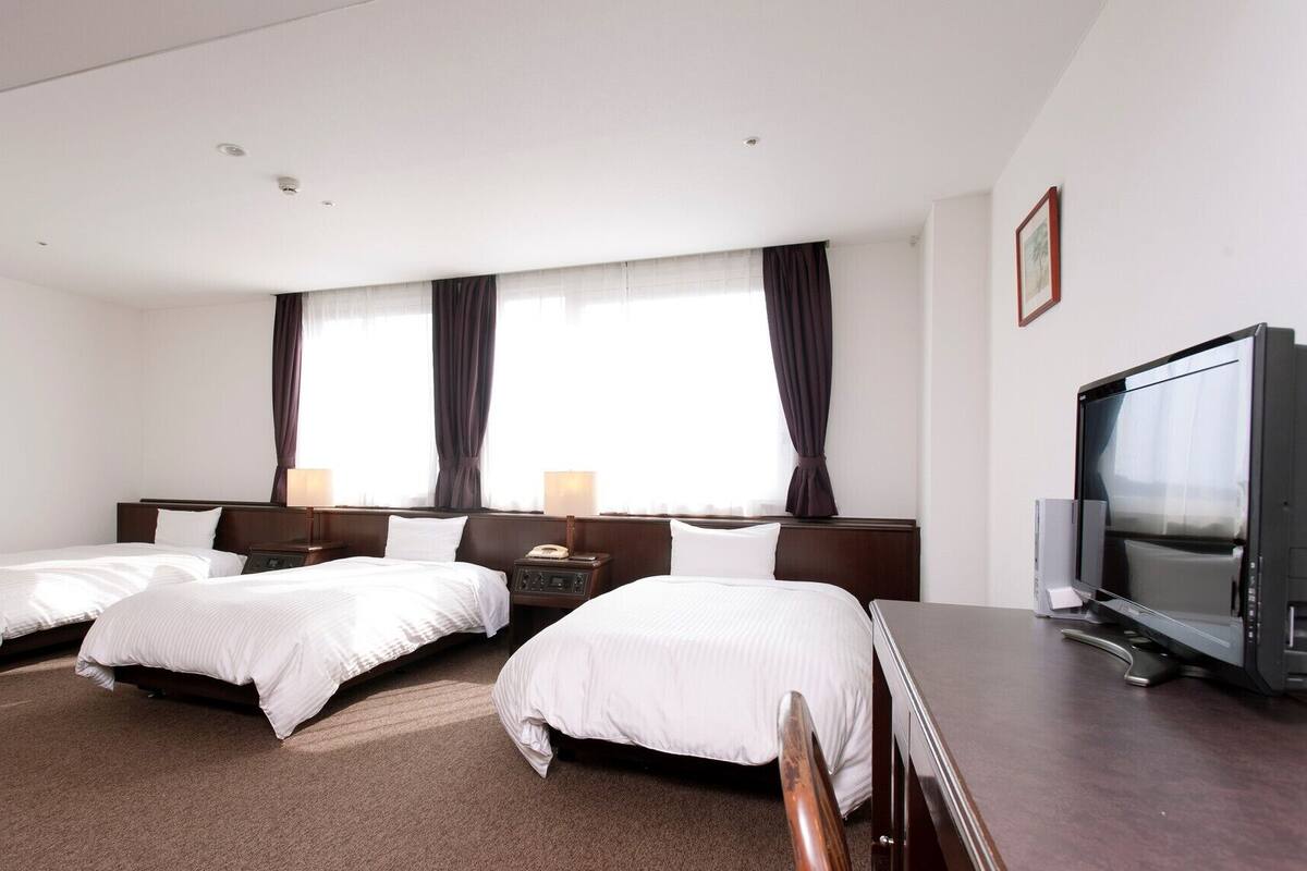 A hotel room with three beds, a television, and a window with curtains.