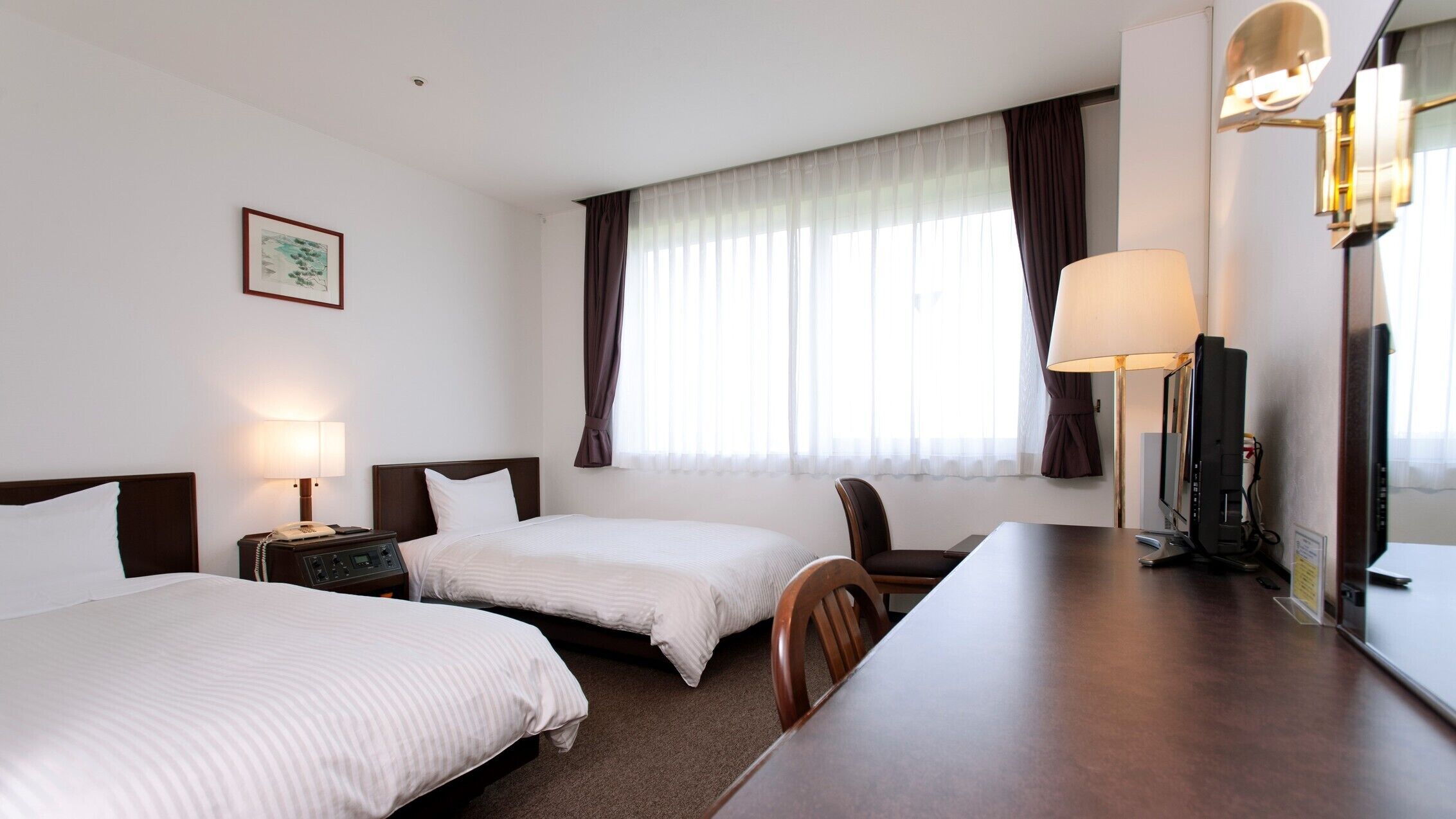 Habitació d'hotel amb dos llits, escriptori, cadira, televisió i finestra amb cortines.