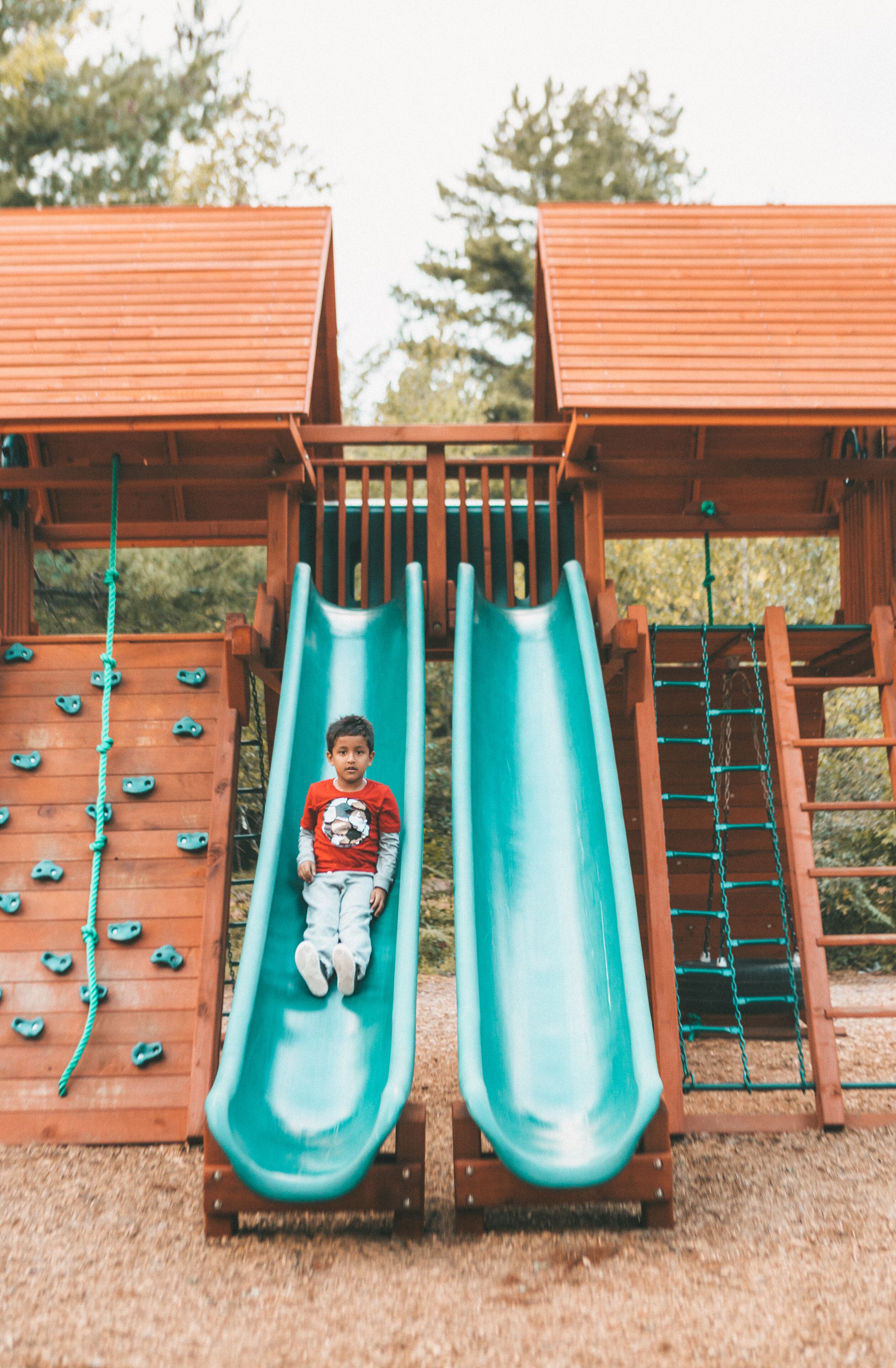 Un enfant sur un toboggan dans un parc pour enfants, avec des murs d’escalade et une structure en bois.