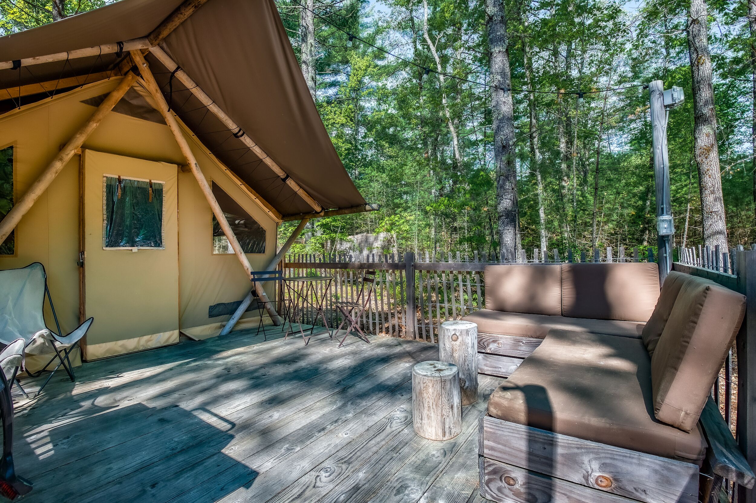 A tent with a wooden deck, a cushioned seating area, and a wooden table.