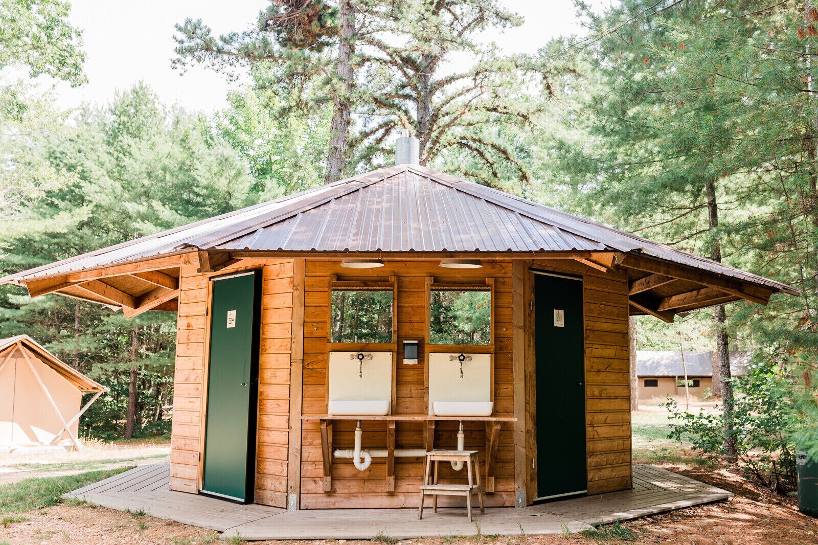 Una cabaña de madera con dos inodoros, un lavamanos y un pequeño taburete.