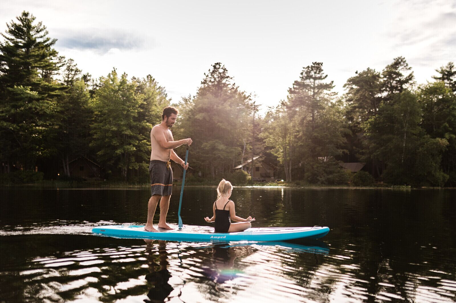 Two people on a paddleboard in a calm lake surrounded by trees.