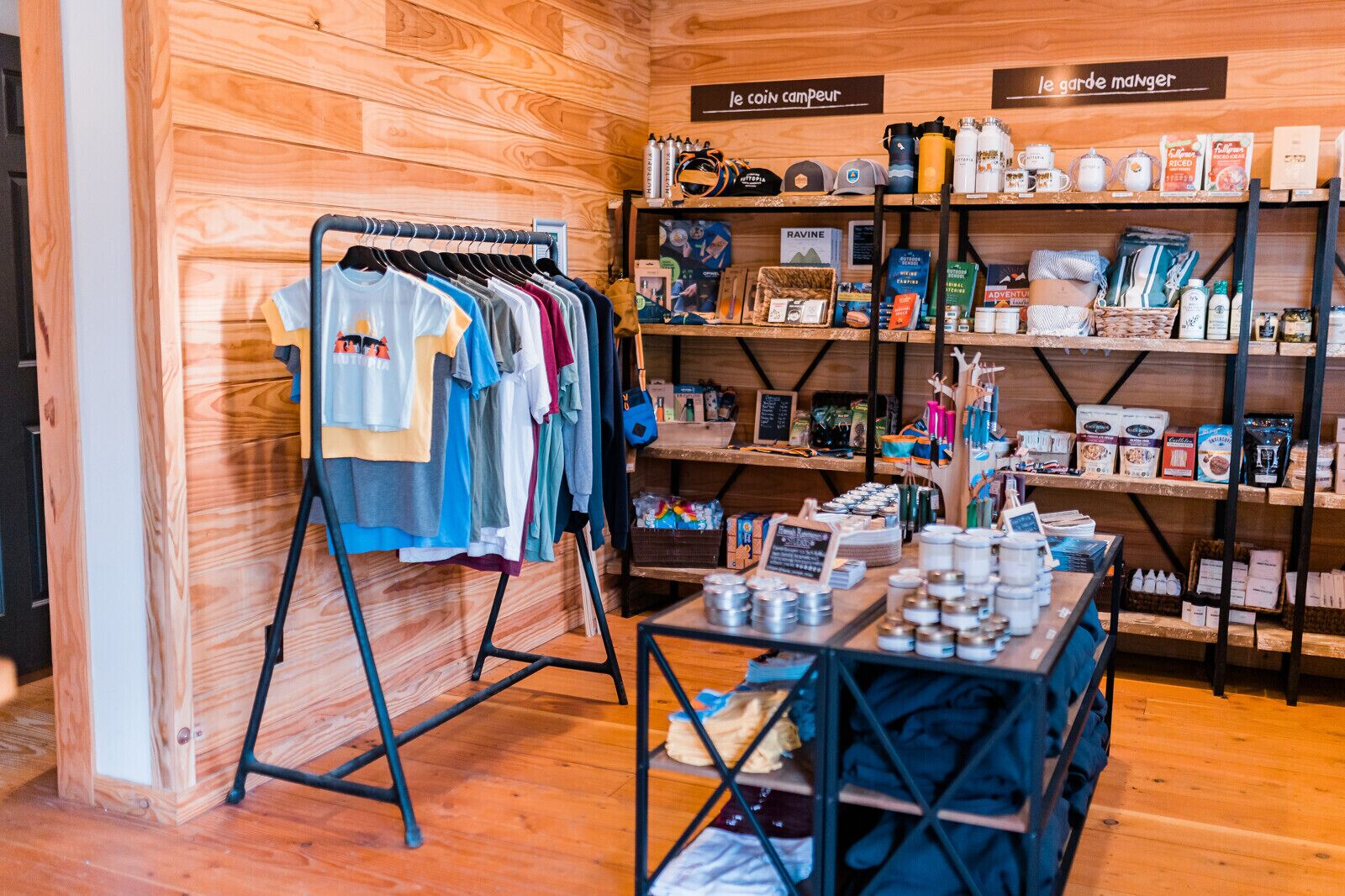 A clothing rack with various shirts, shelves with food items, and a table with jars.