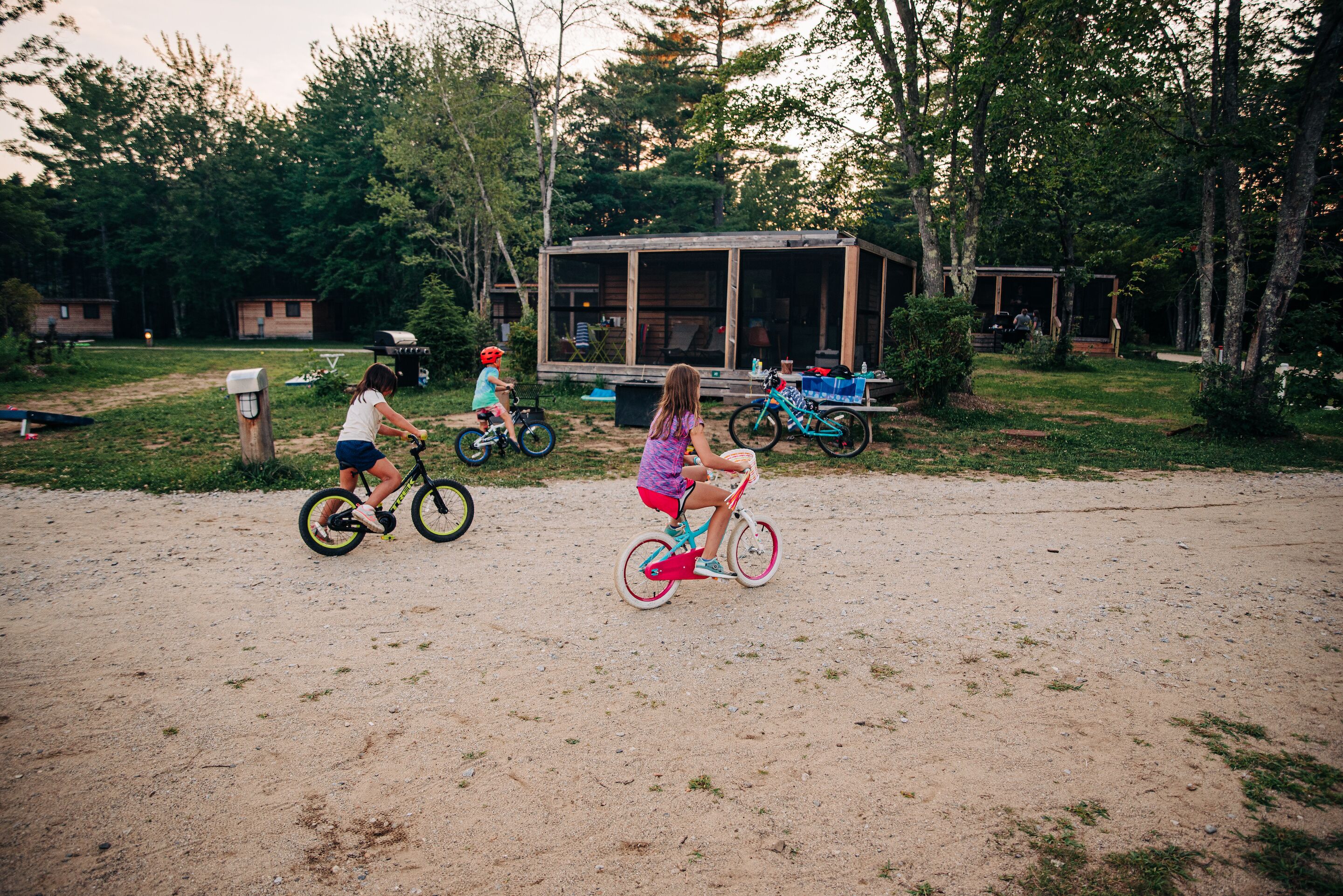 A campsite with a wooden cabin, bicycles, and a dirt ground.