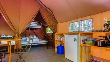 A compact, well-equipped tent with bunk beds, a small kitchenette, and a window overlooking a forest.