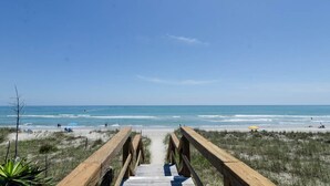Un muelle de madera que conduce a una playa con cielos despejados y aguas tranquilas.
