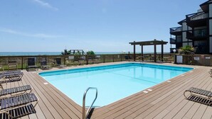 Zona de piscina con sillas de descanso y un muelle de madera, con vista al océano.