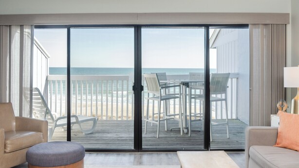 Una habitaci ón con un gran ventanal corredizo que da a un balcón con vistas a la playa.