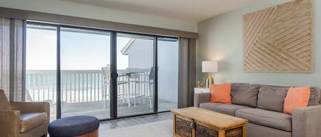 A spacious living room with a sliding glass door leading to a balcony, a sofa, a coffee table, and a chair.