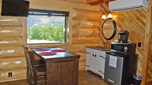 Interior de una cabaña de madera con una mesa de comedor, sillas, un lavamanos, una estufa, una cafetera y un equipo de aire acondicionado.