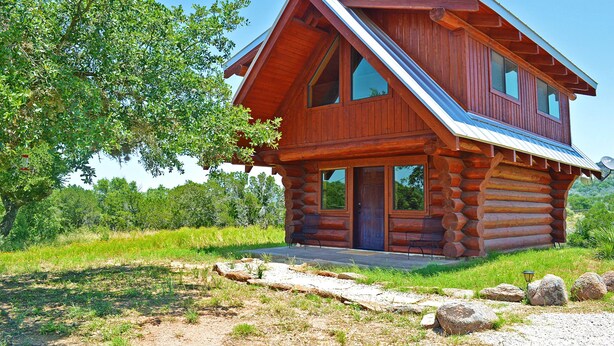Una cabaña de troncos con techo inclinado, ventanas amplias y una puerta principal.