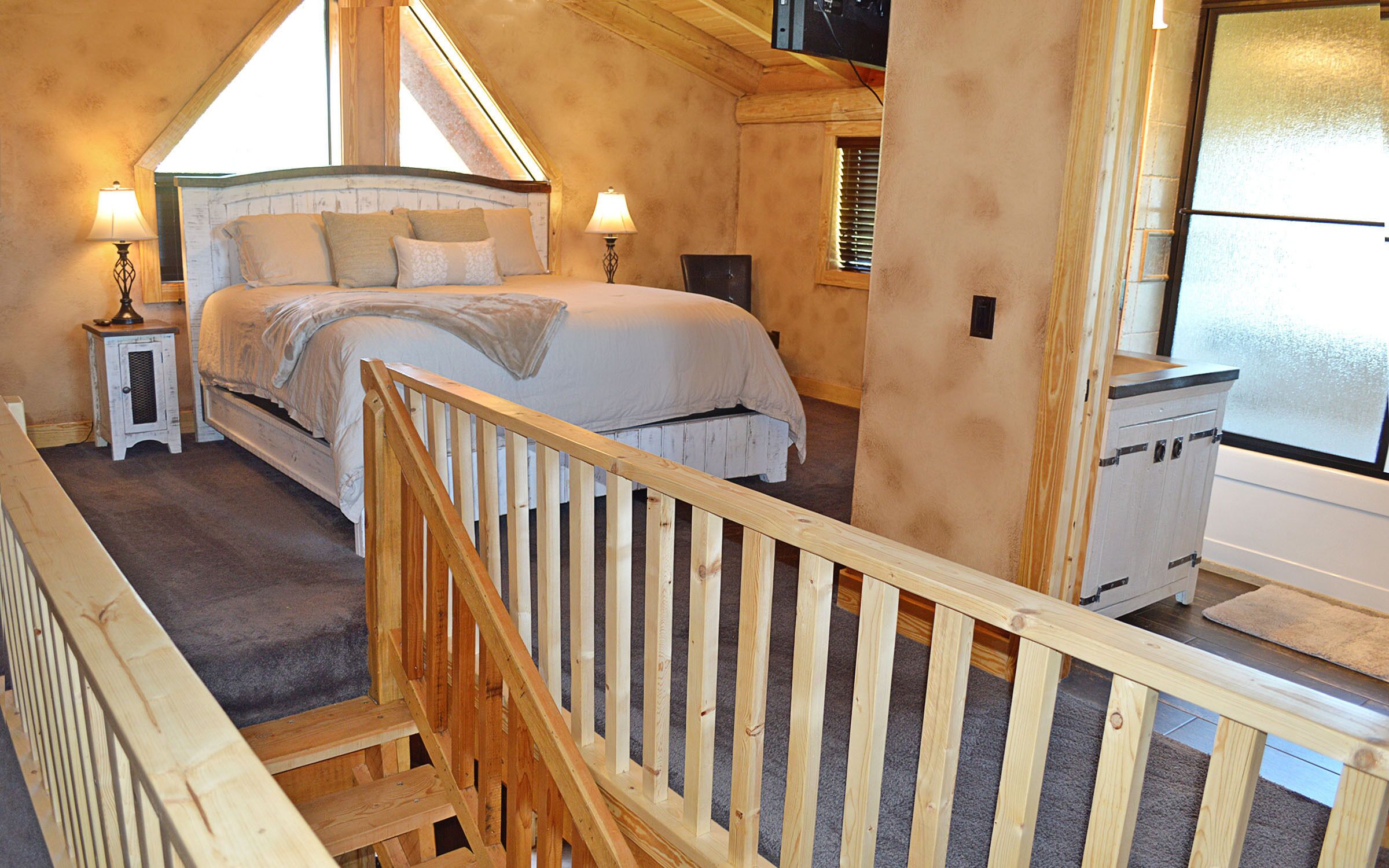 A bedroom with a wooden bed, two bedside lamps, a window with blinds, and a view of the outside.
