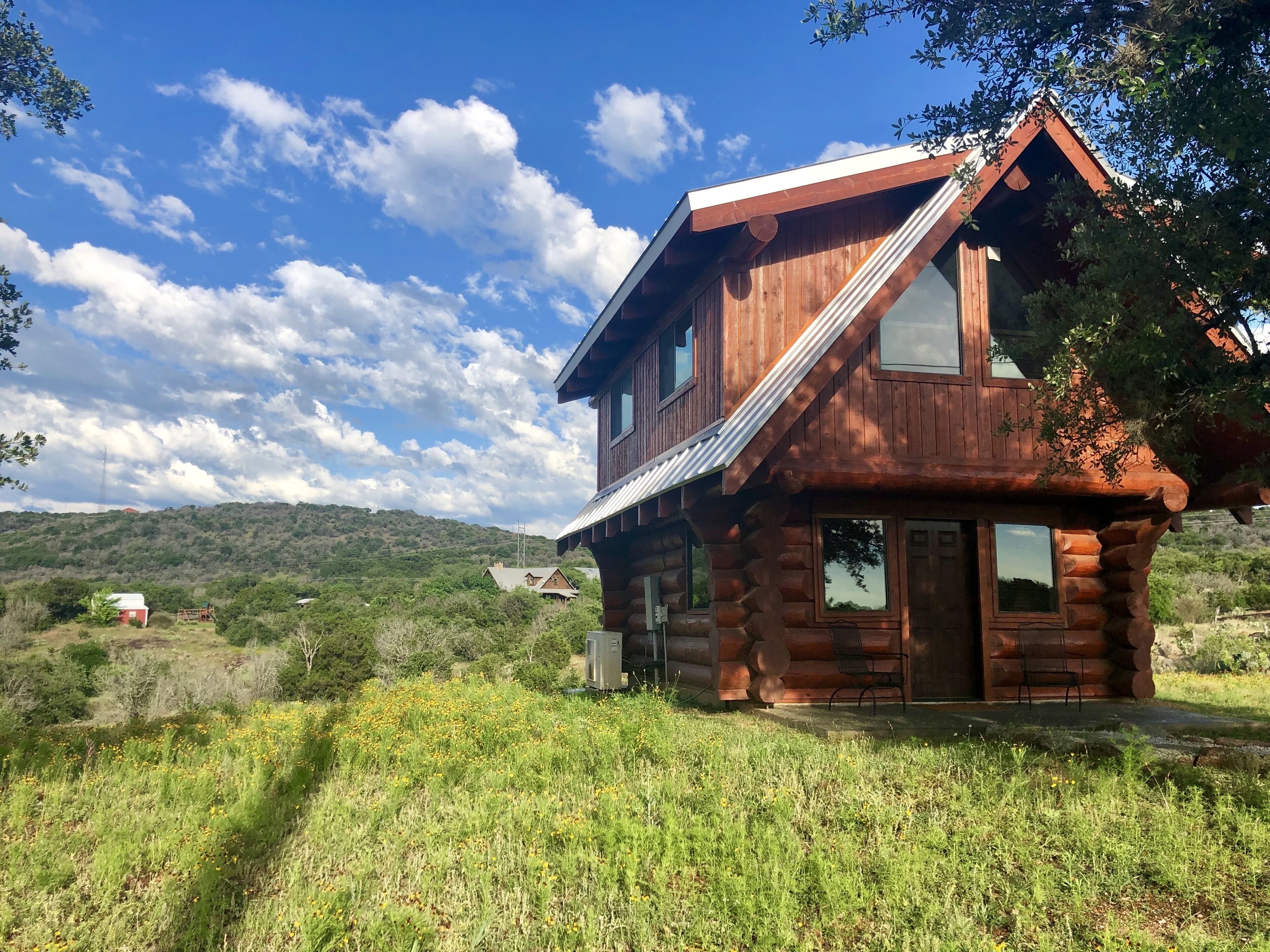 A rustic log cabin with a sloped roof, large windows, and a front porch with chairs.