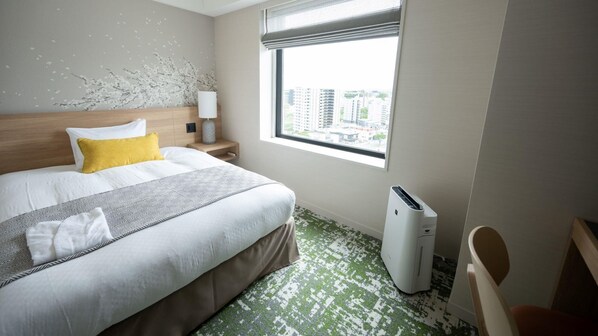 Une chambre d’hôtel comprenant un lit, une table de chevet, une lampe, une fenêtre donnant sur la ville et un radiateur mobile.