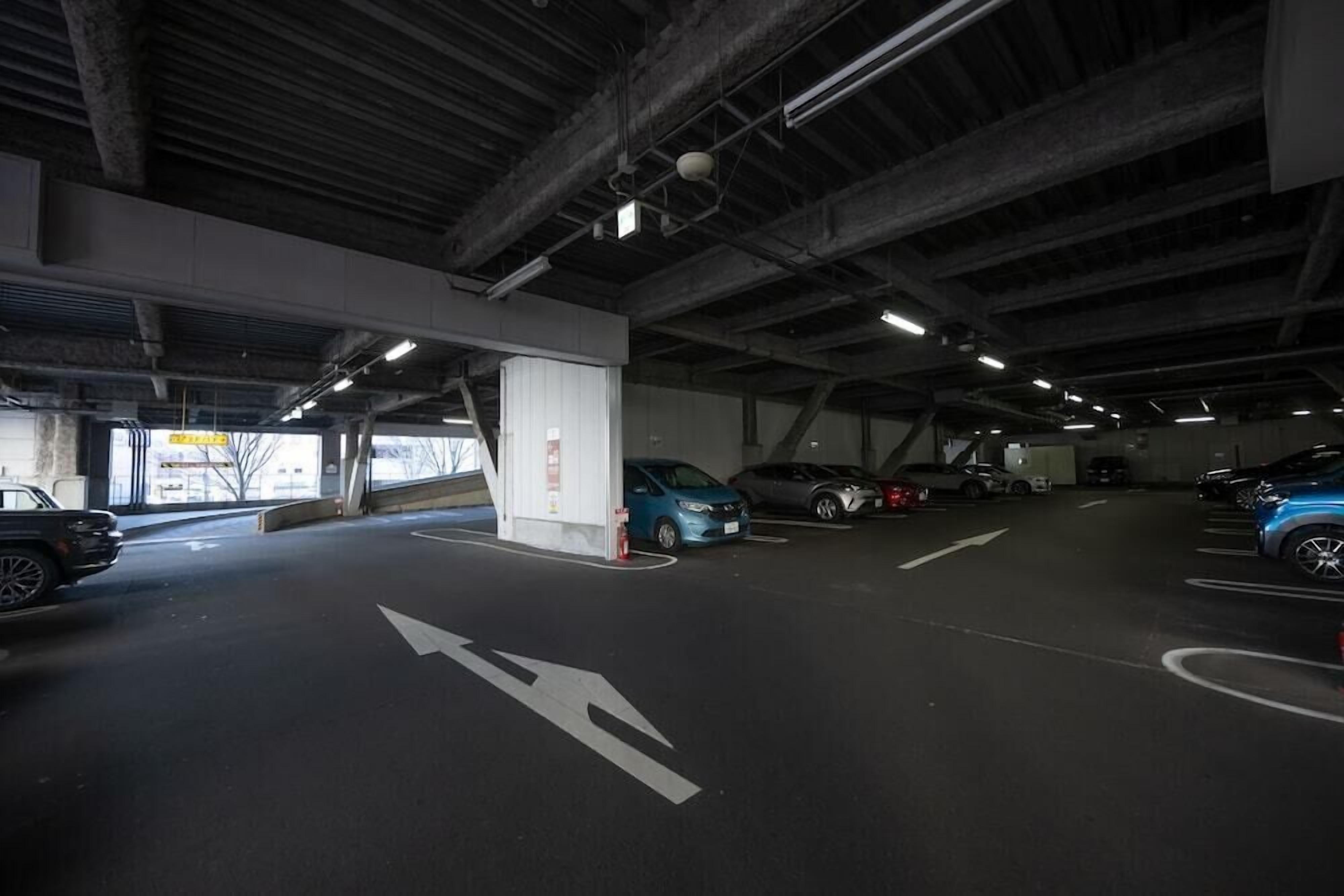 An underground parking garage with multiple parking spaces, directional arrows on the floor, and a few cars parked.