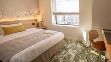 A hotel room with a bed, a desk, a chair, a window with a city view, and a wall with a textured design.
