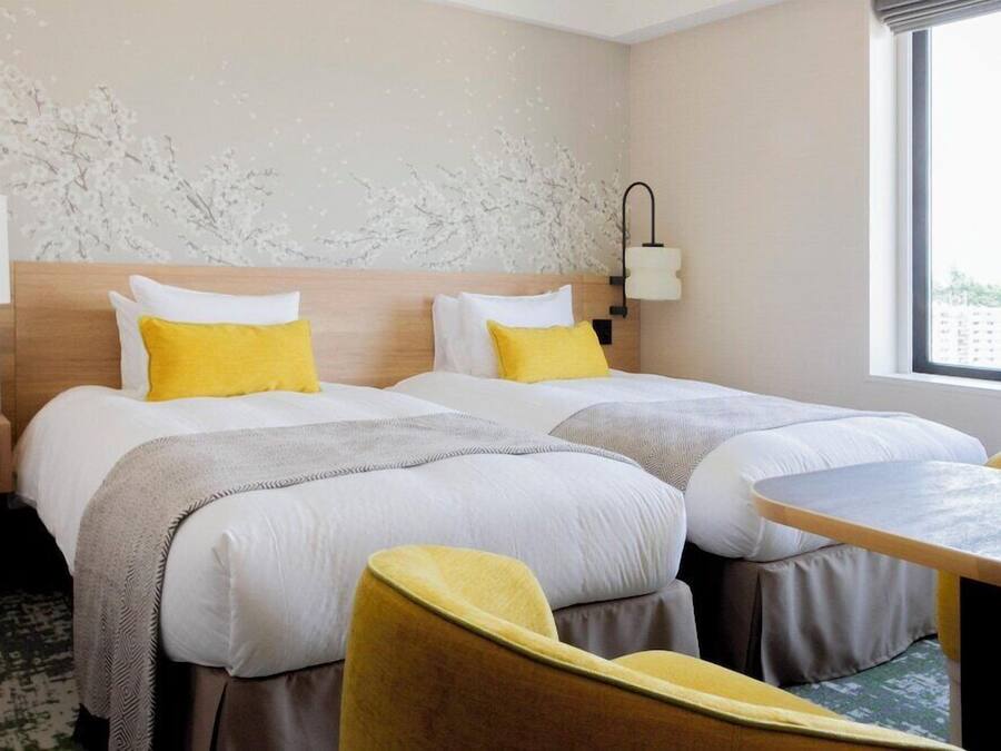 A hotel room with two beds, a small table, and a chair.