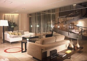 Un salon moderne avec un escalier en colimaçon, un canapé blanc, une table basse et une grande fenêtre avec des rideaux.