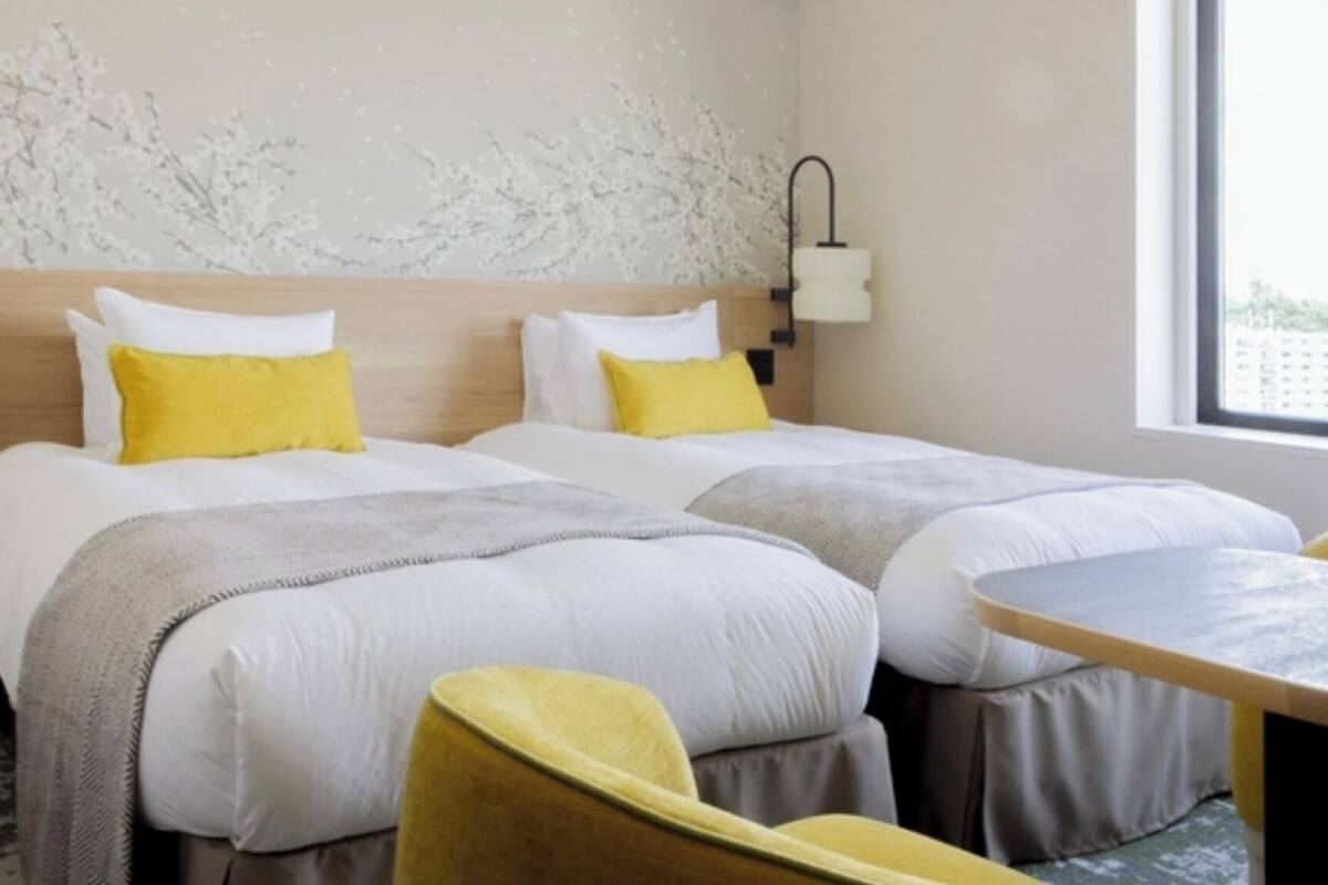 A hotel room with two beds, a small table, a chair, and a window.