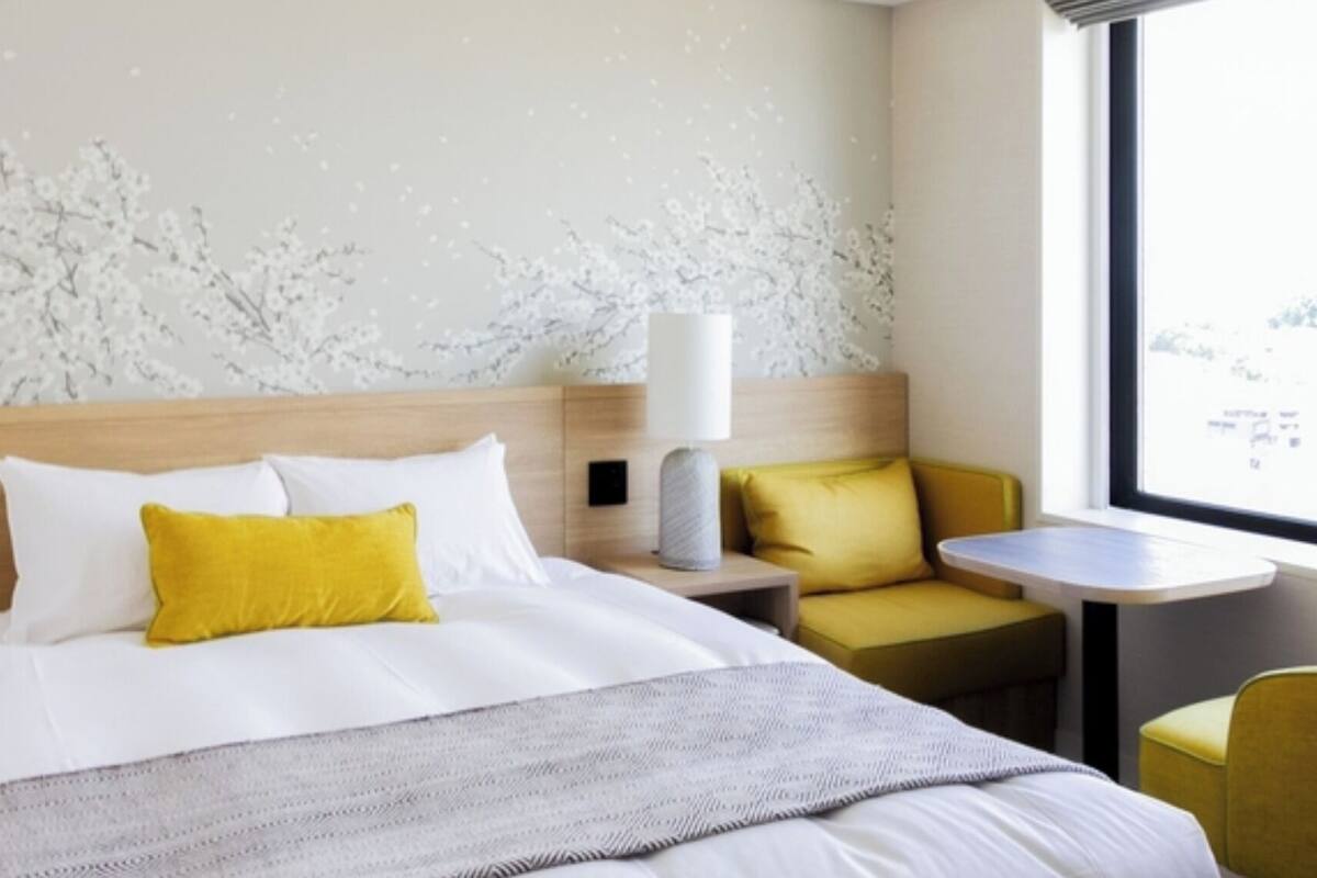A hotel room with a bed, bedside table, lamp, and a small table with a chair.