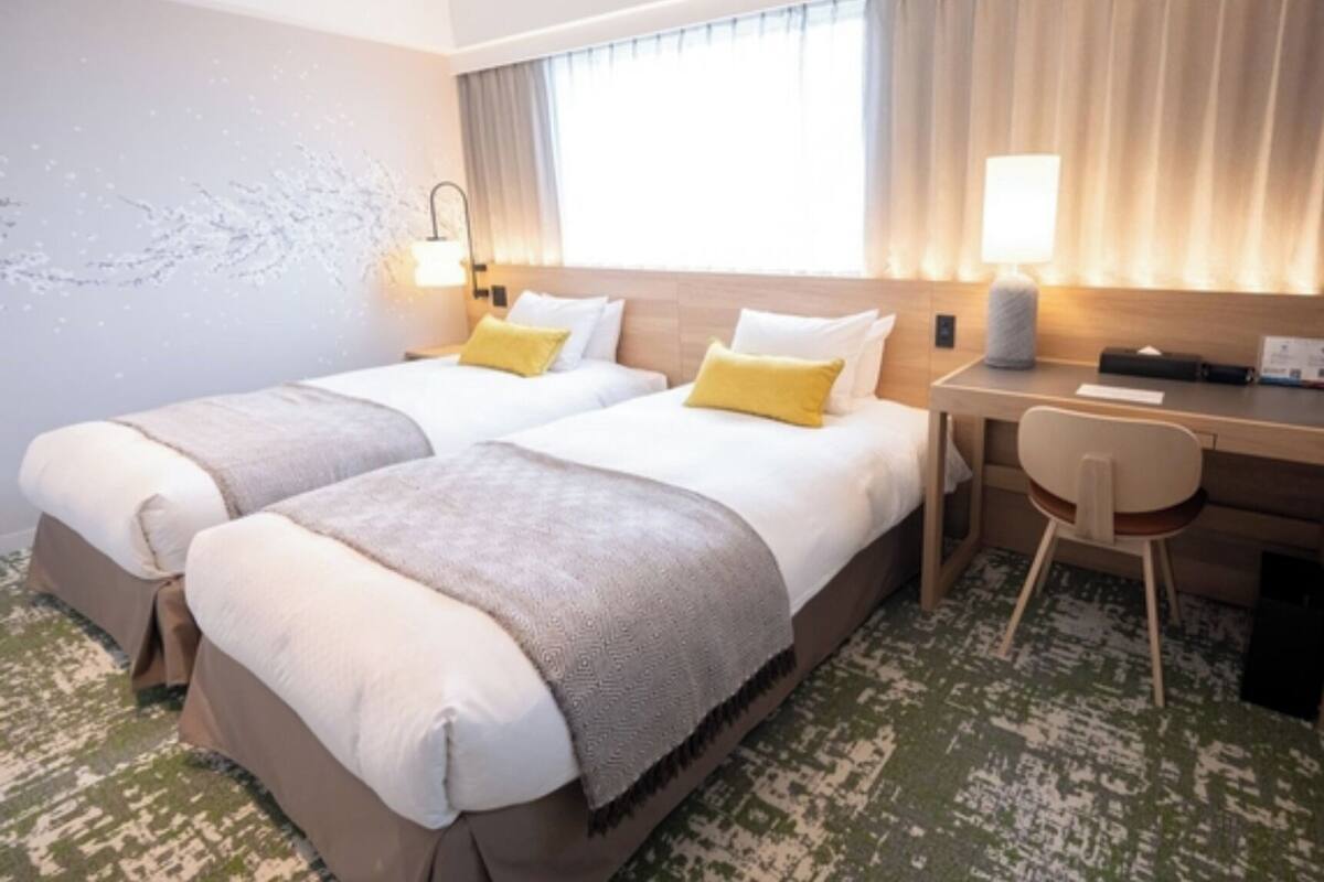 A hotel room with two beds, a desk, and a chair.