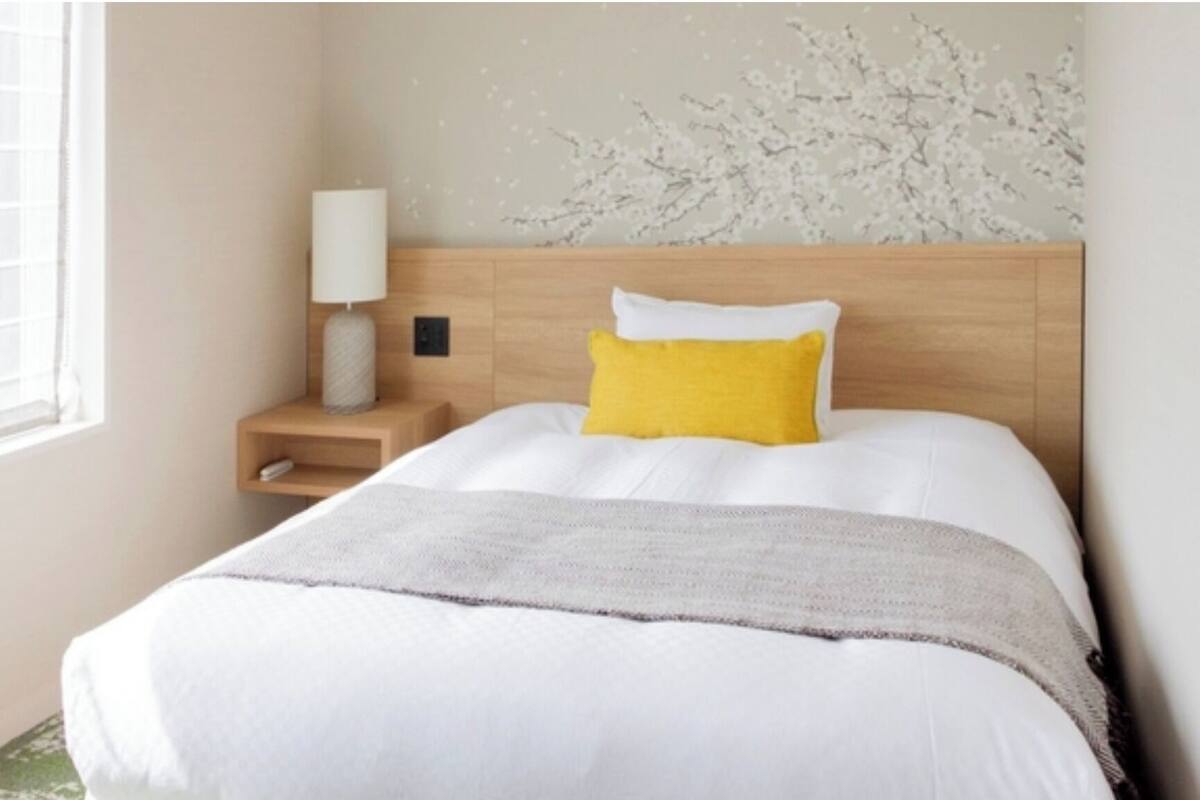 A hotel room with a bed, a nightstand, a lamp, and a wall with a floral pattern.