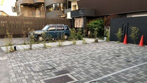 Une zone extérieure pavée où est garée une voiture, avec un regard d’égout et un bâtiment à la façade sombre portant une enseigne.