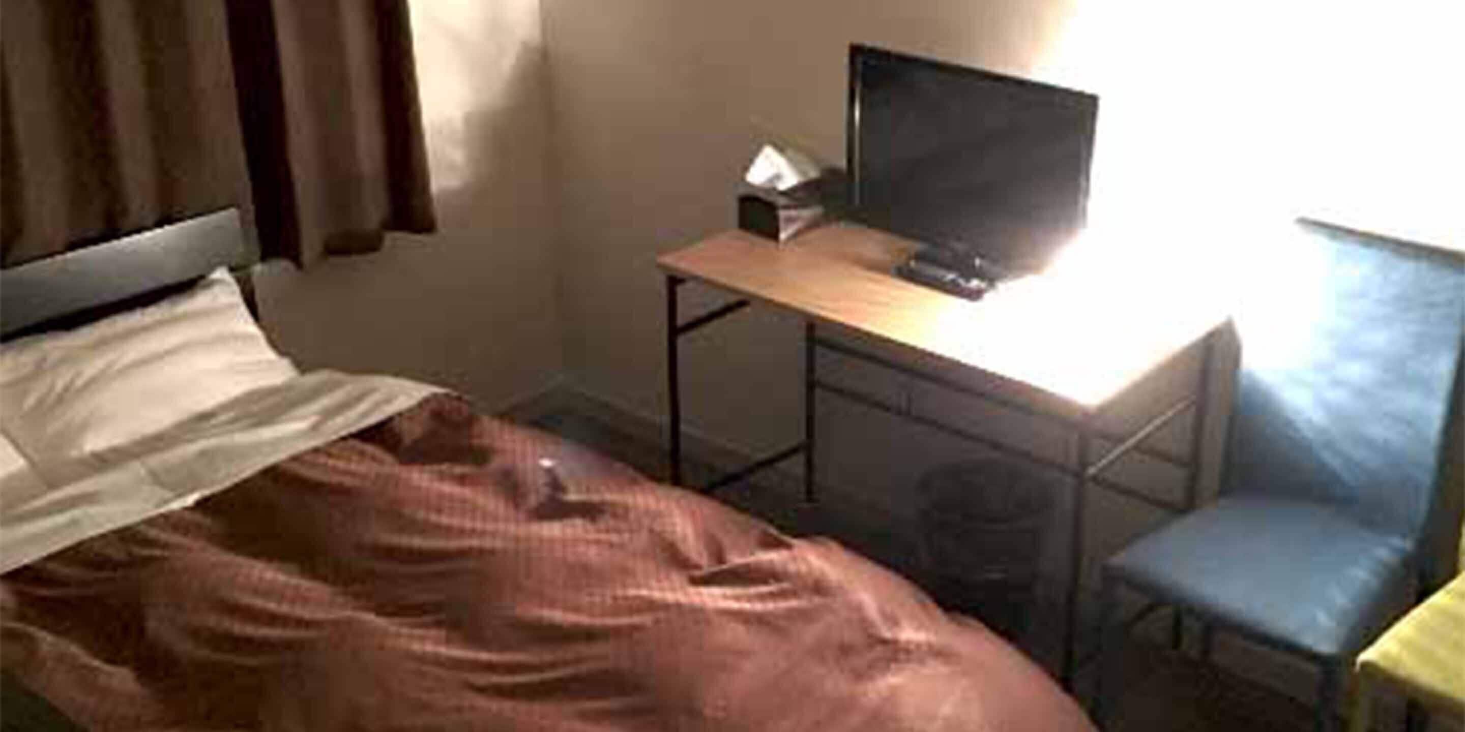 A bedroom with a bed, a desk with a computer, a chair, and a window.