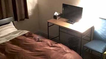 A bedroom with a bed, a desk with a computer, a chair, and a window.