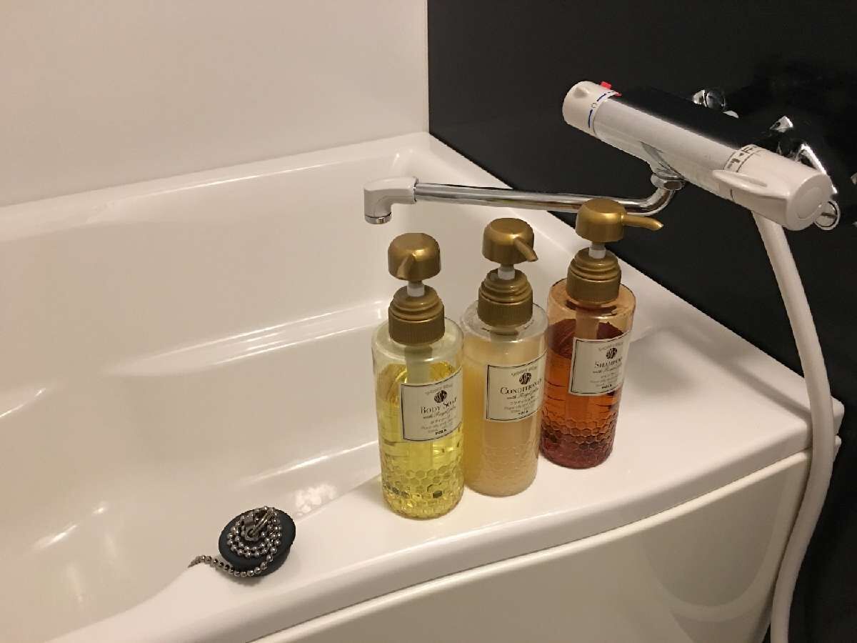 A bathtub with three bottles of body wash and a loofah.