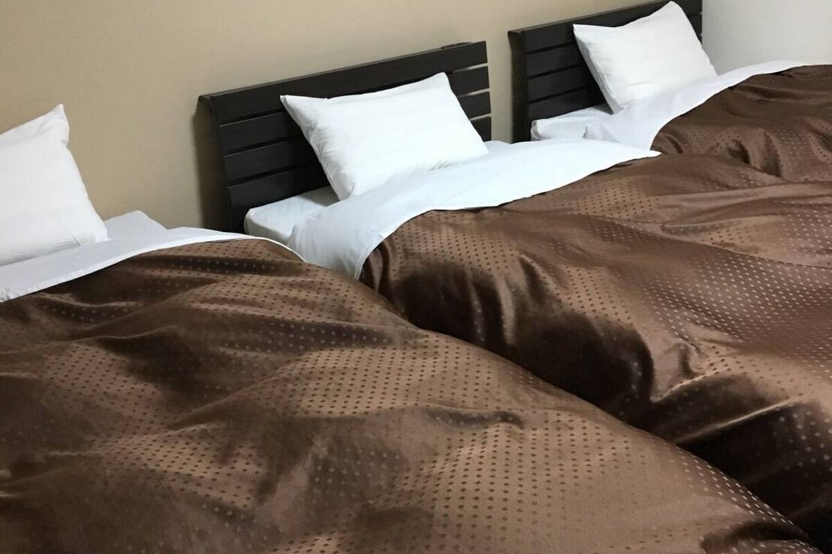 Una habitación de hotel con una cama, ropa de cama blanca y una manta marrón.