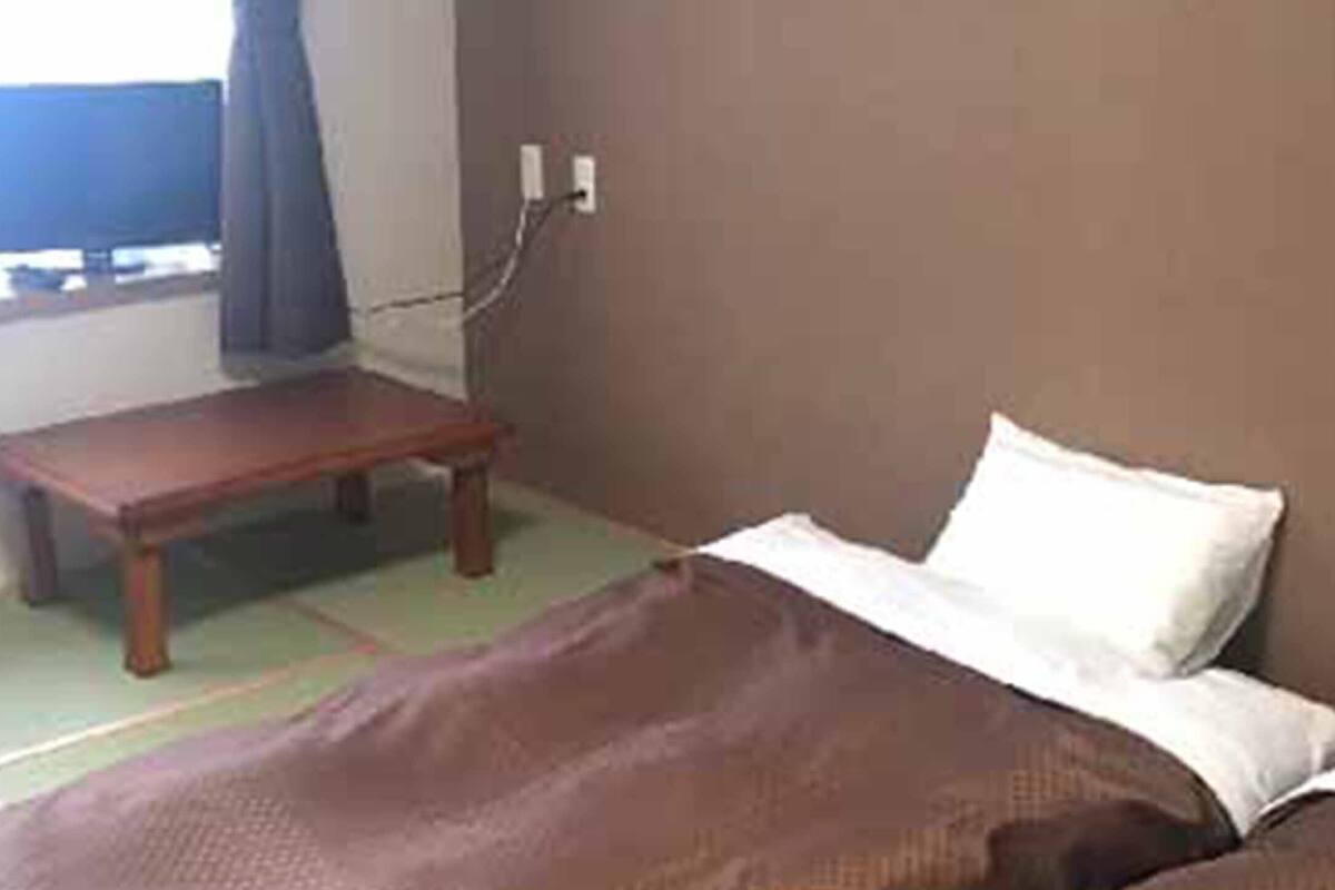Una habitación con una cama, una mesita de madera y un enchufe en la pared.