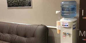 Ein Zimmer mit einem braunen Ledersofa, einem Wasserspender und einer an der Wand montierten Elektroverteilung.