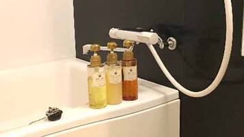 Un baño con bañera, ducha de mano y tres botellas de jabón líquido.