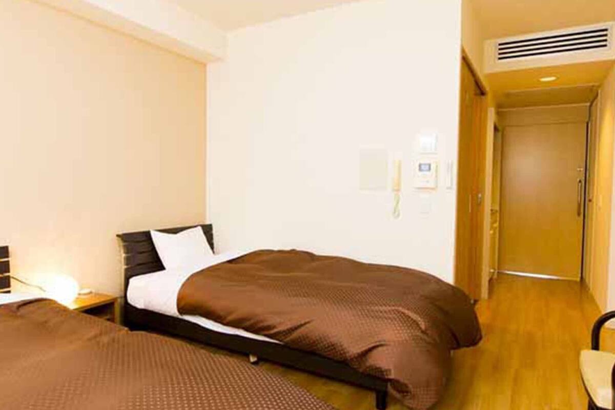 Habitación de hotel con dos camas, piso de madera, una mesita y una puerta que da a otra habitación.