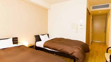 Quarto de hotel com duas camas, piso de madeira, uma mesa pequena e uma porta que dá para outro aposento.