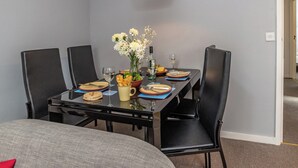 Een eethoek met een tafel voor vier personen, zwarte stoelen, een rode hanglamp en een vaas met bloemen.