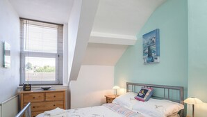 Een slaapkamer met een bed, twee nachtkastjes, een raam met jaloezieën, een radiator en een schilderij aan de muur.