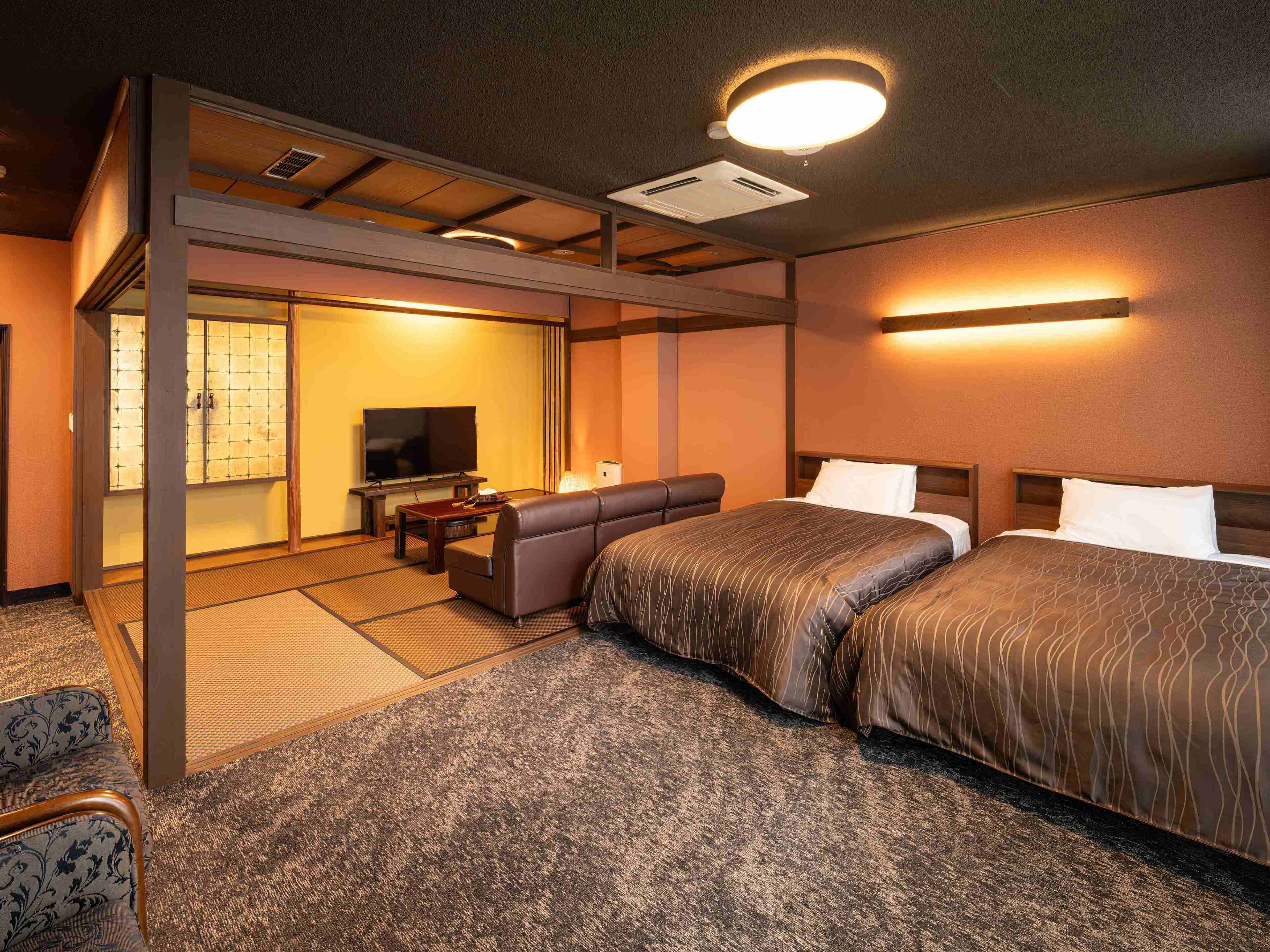 Een hotelkamer met een bank, twee bedden, een televisie en een traditionele Japanse schuifdeur.