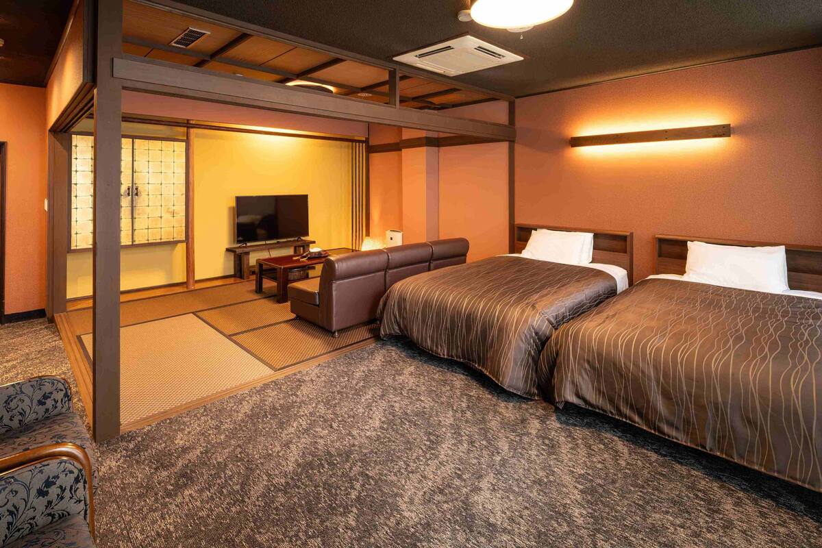 A hotel room with a sofa, two beds, a TV, and a traditional Japanese sliding door.