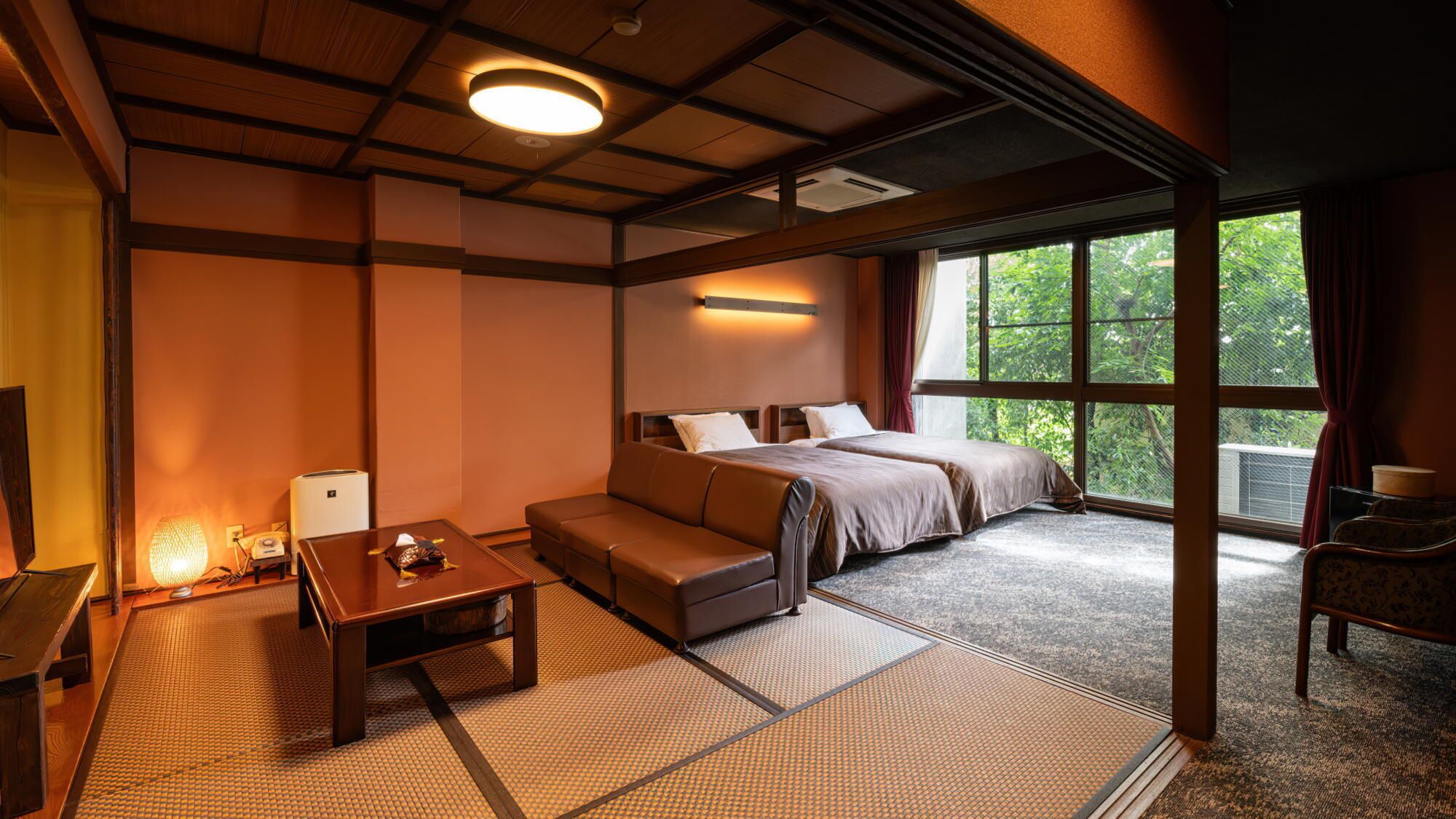 Een hotelkamer met een bed, een bank en een kleine tafel. Er is een raam met uitzicht op groen.