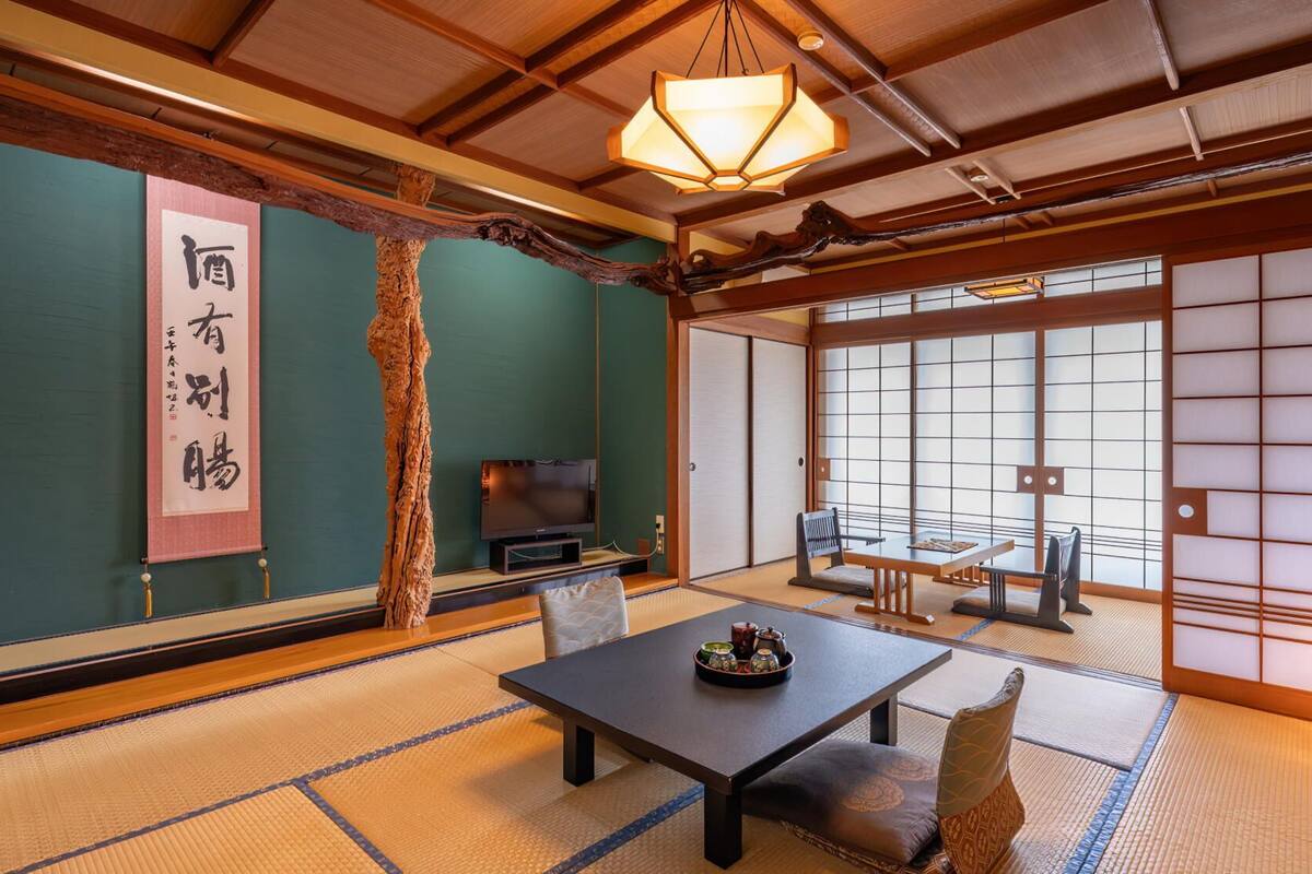 A traditional Japanese room with tatami flooring, a low table with tea set, a television, and sliding shoji doors.
