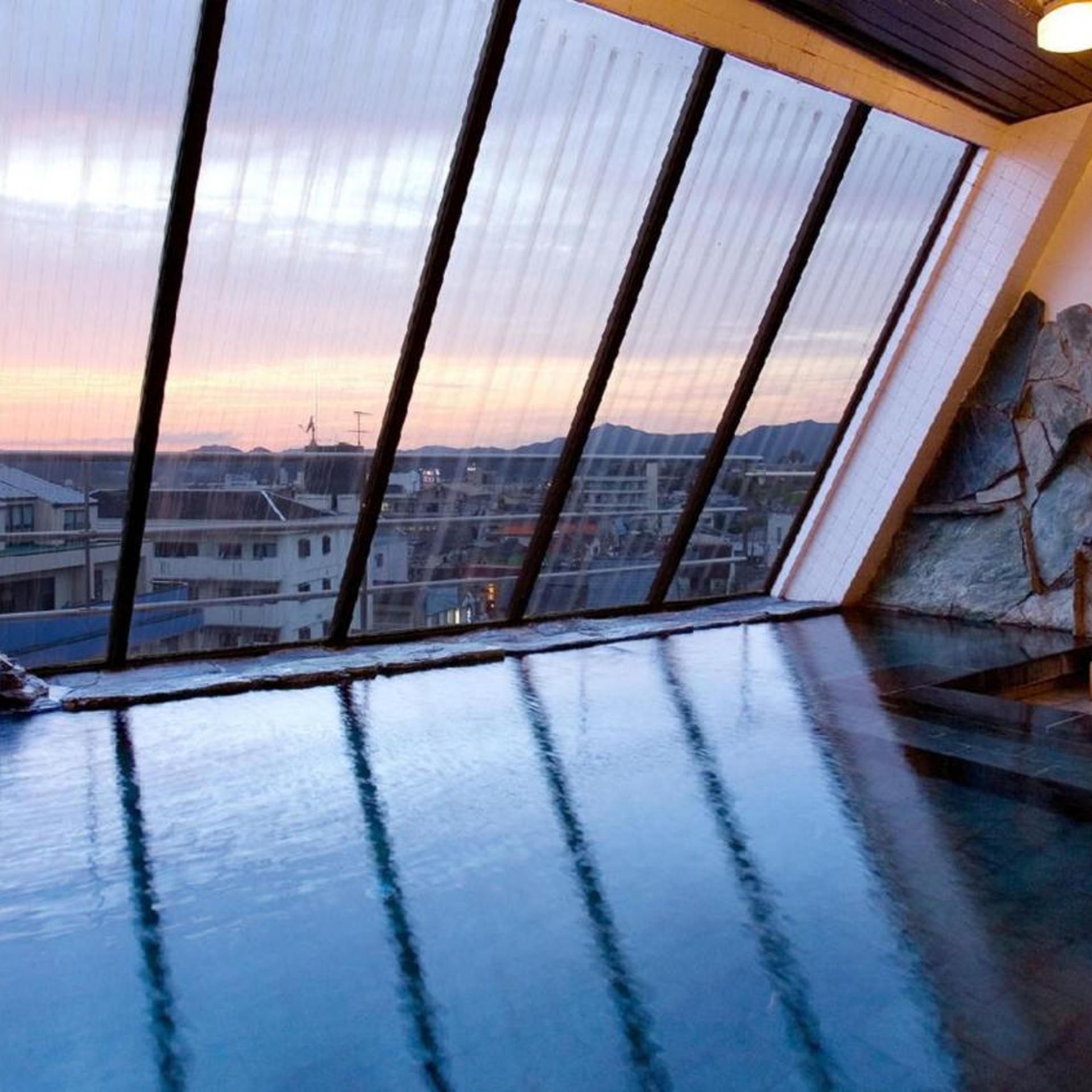Una habitación con un amplio ventanal con vistas a un paisaje urbano al atardecer.